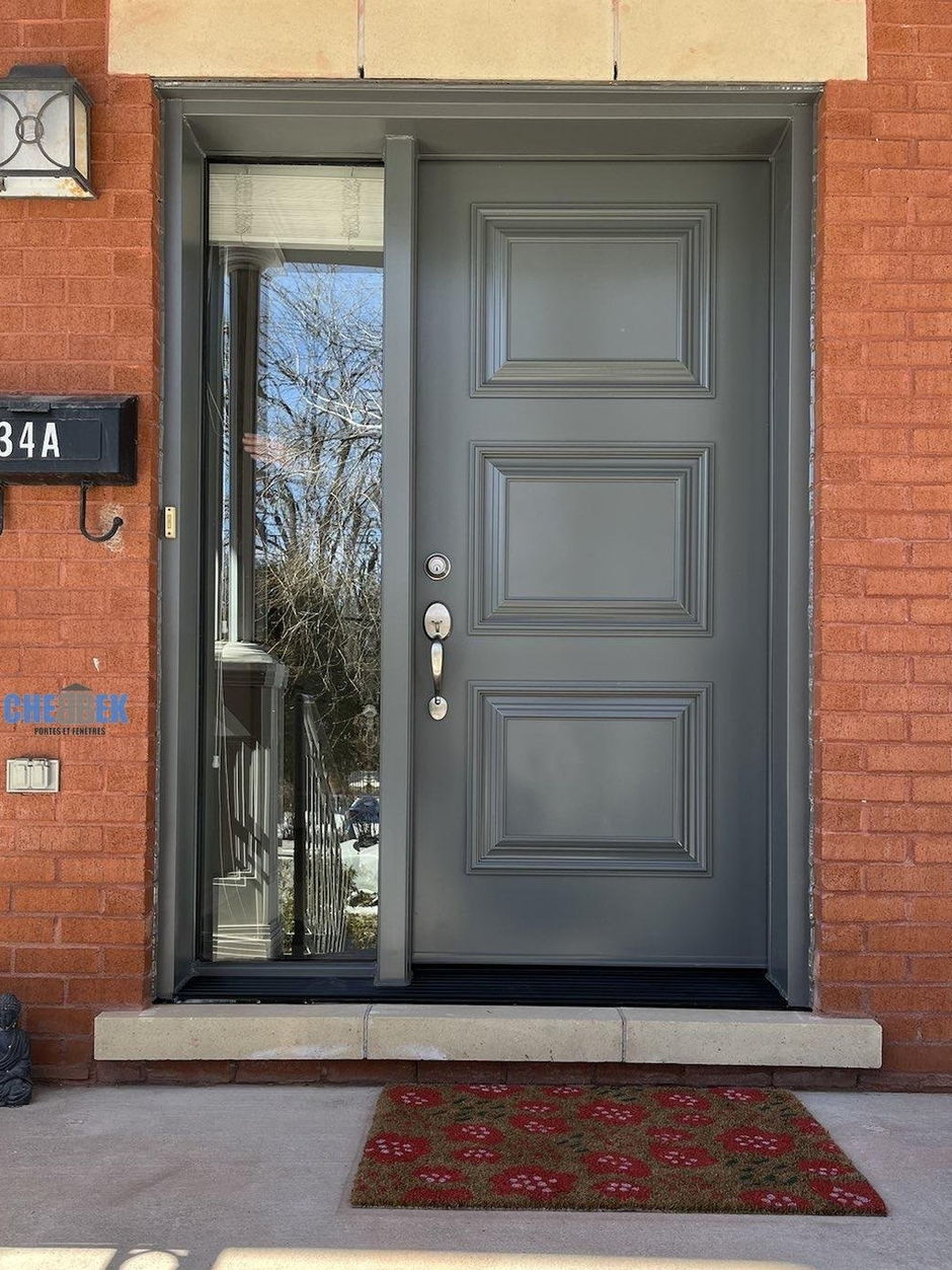 Grey entry door with a glass sidelight on a red brick front, installed by CHEBBEK