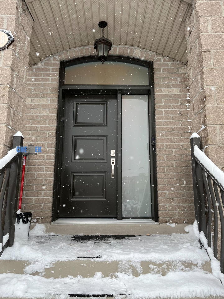 Black entry door with a sidelight and glass transom, in winter