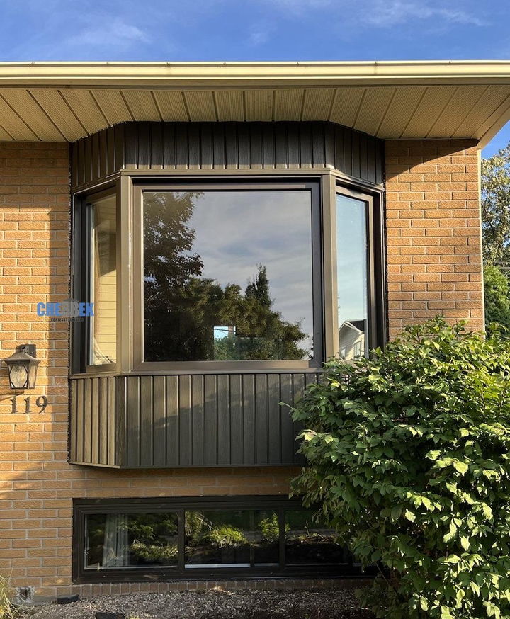 Fenêtre en baie avec revêtement vert sur une façade de brique jaune